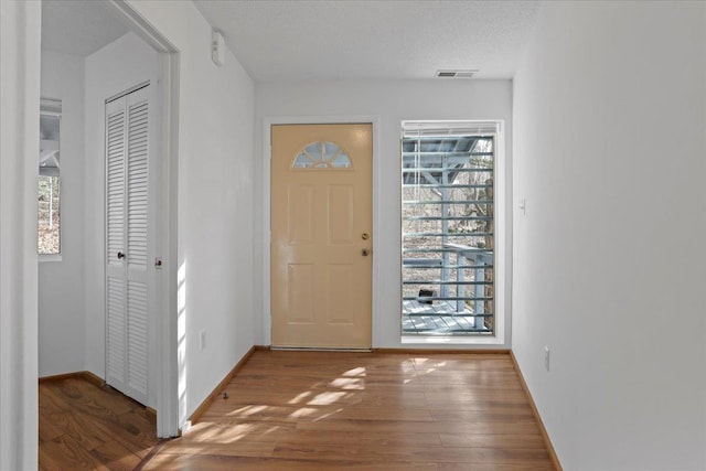 foyer with baseboards, visible vents, and wood finished floors