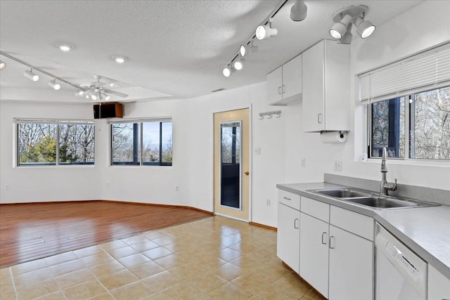 kitchen with white dishwasher, a textured ceiling, a sink, rail lighting, and open floor plan