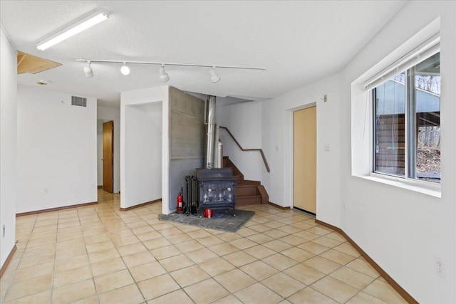 below grade area featuring stairs, a wood stove, track lighting, visible vents, and baseboards