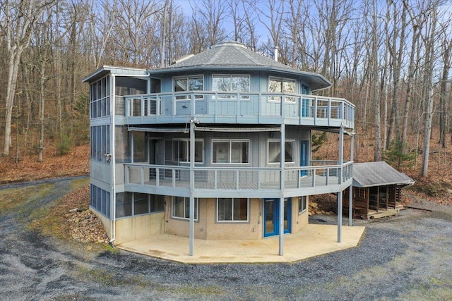 rear view of house featuring a balcony, a wooded view, a patio, and a sunroom