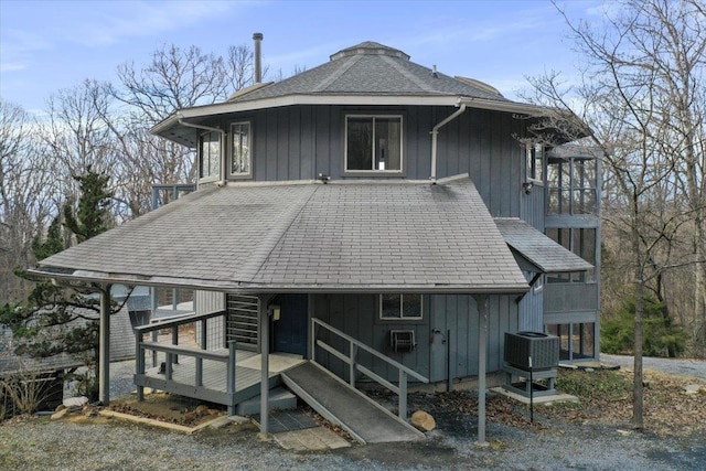 back of house with central AC unit, board and batten siding, a shingled roof, and a balcony