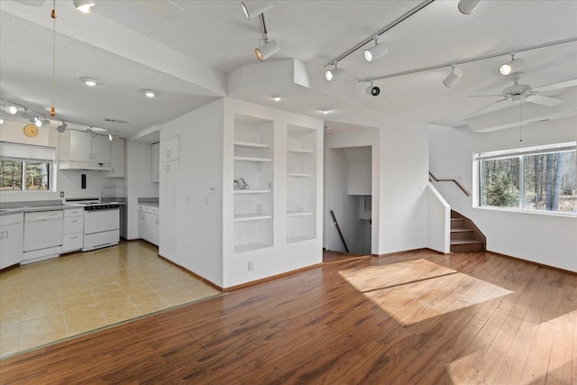 unfurnished living room with stairway, a textured ceiling, and track lighting