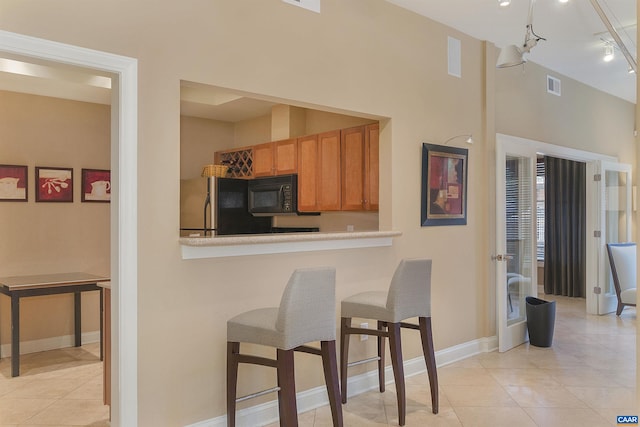 kitchen with refrigerator, black microwave, track lighting, light tile patterned floors, and a breakfast bar area