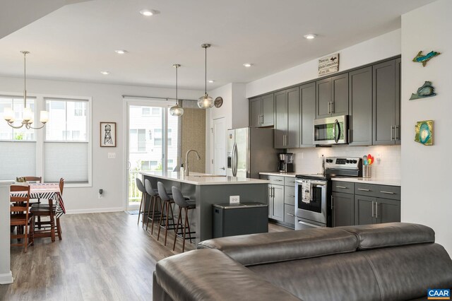 kitchen with stainless steel appliances, a chandelier, a kitchen island with sink, light countertops, and recessed lighting