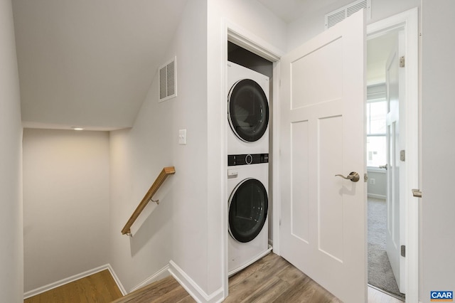 washroom with stacked washing machine and dryer, wood finished floors, and baseboards