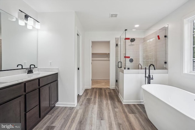 bathroom with wood finished floors, a freestanding tub, a shower stall, vanity, and a spacious closet