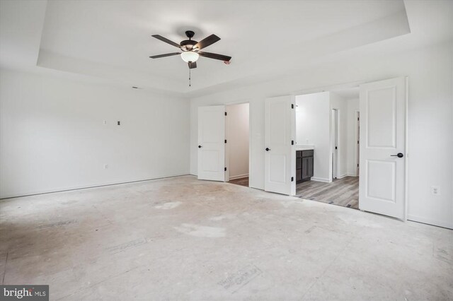 unfurnished bedroom with a tray ceiling, ensuite bathroom, and ceiling fan
