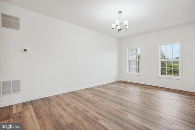 spare room featuring a chandelier, wood finished floors, and baseboards