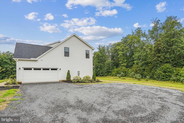 view of side of home with roof with shingles and gravel driveway