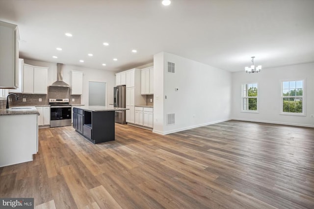 kitchen featuring stainless steel appliances, wall chimney range hood, a sink, a chandelier, and wood finished floors