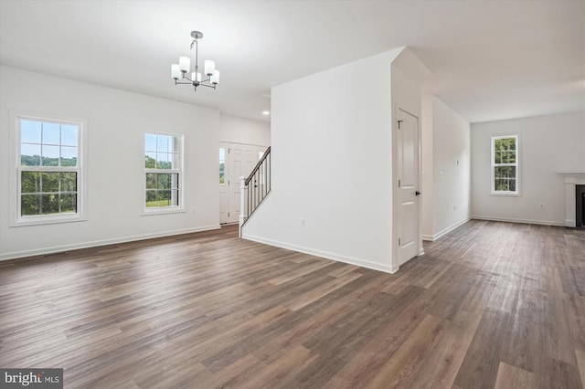 unfurnished living room with a chandelier, stairway, healthy amount of natural light, and dark wood-style floors