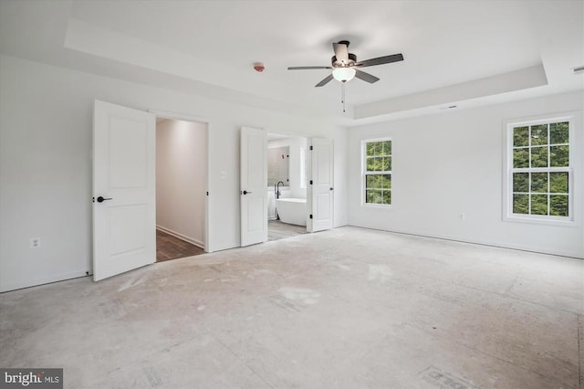 unfurnished bedroom with a raised ceiling, ensuite bathroom, a ceiling fan, and baseboards