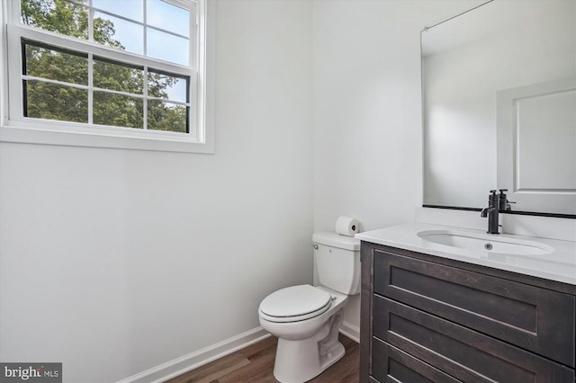half bathroom featuring wood finished floors, toilet, baseboards, and vanity