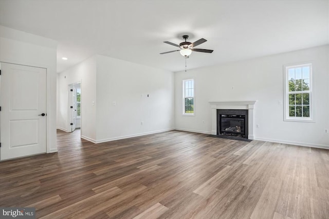 unfurnished living room featuring ceiling fan, wood finished floors, a fireplace with flush hearth, and baseboards