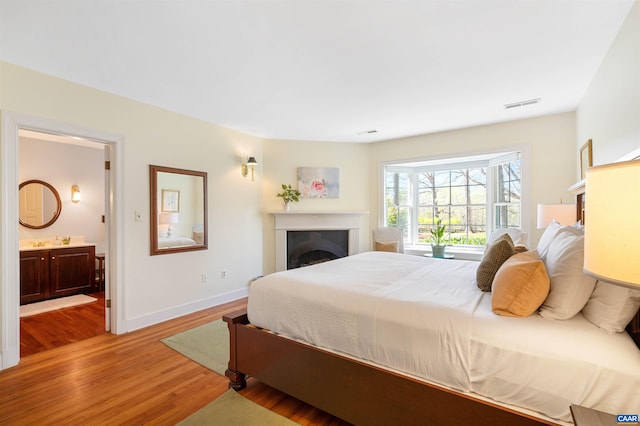 bedroom featuring wood finished floors, a fireplace, ensuite bathroom, visible vents, and baseboards