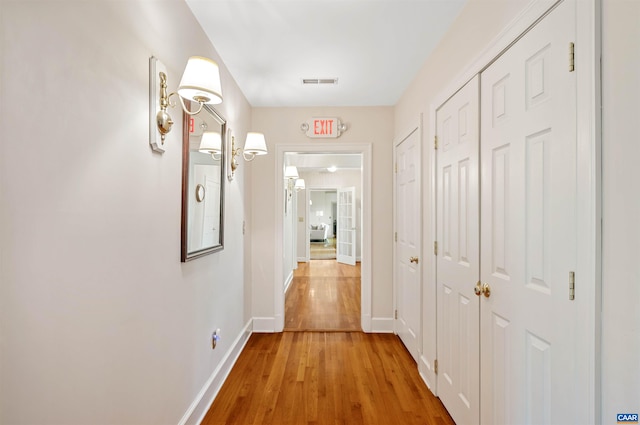 hall with baseboards, visible vents, and light wood-type flooring
