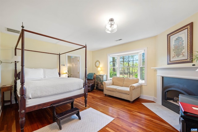 bedroom featuring baseboards, a fireplace with flush hearth, visible vents, and wood finished floors