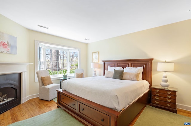 bedroom with light wood finished floors, visible vents, baseboards, and a fireplace