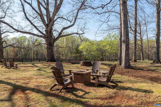 view of yard featuring a fire pit, fence, and a view of trees