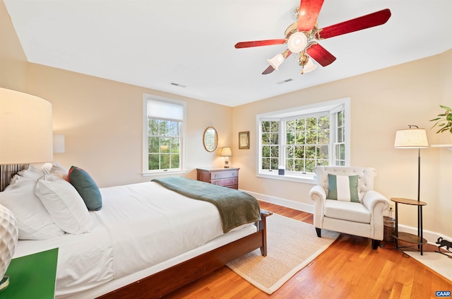 bedroom with multiple windows, visible vents, wood finished floors, and baseboards