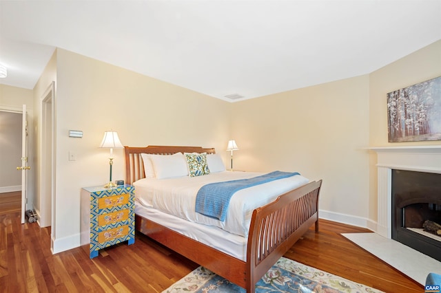 bedroom with visible vents, wood finished floors, baseboards, and a fireplace with flush hearth