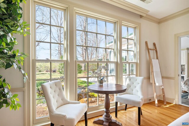 sitting room with light wood-type flooring, visible vents, and ornamental molding