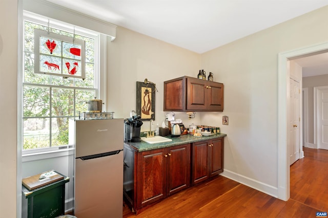 kitchen featuring freestanding refrigerator, baseboards, dark wood finished floors, a sink, and dark countertops