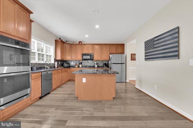 kitchen featuring a sink, light wood finished floors, stainless steel appliances, backsplash, and a kitchen island