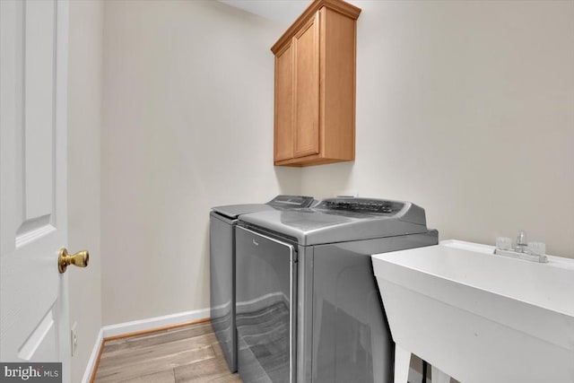 washroom featuring washing machine and dryer, light wood-style floors, baseboards, a sink, and cabinet space