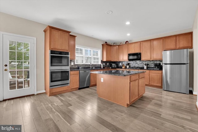 kitchen with backsplash, stainless steel appliances, light wood-type flooring, and a center island