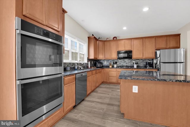 kitchen featuring decorative backsplash, dark stone countertops, a sink, light wood finished floors, and appliances with stainless steel finishes