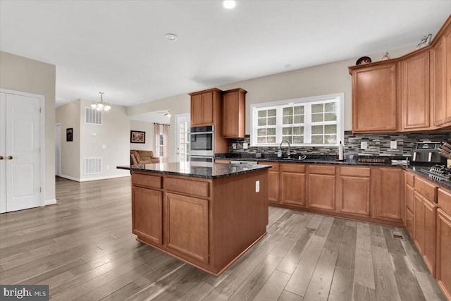 kitchen with an inviting chandelier, visible vents, light wood-style floors, a center island, and backsplash