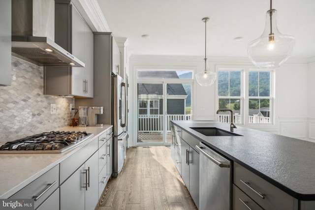 kitchen with wall chimney exhaust hood, appliances with stainless steel finishes, gray cabinetry, light wood-style floors, and a sink