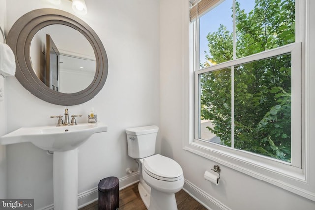 half bathroom with baseboards, wood finished floors, and toilet