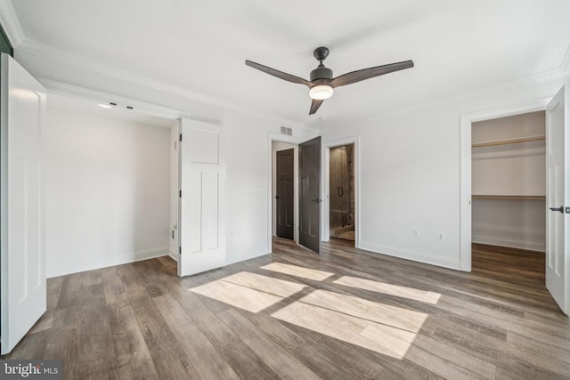 unfurnished bedroom with a walk in closet, ornamental molding, wood finished floors, a closet, and baseboards