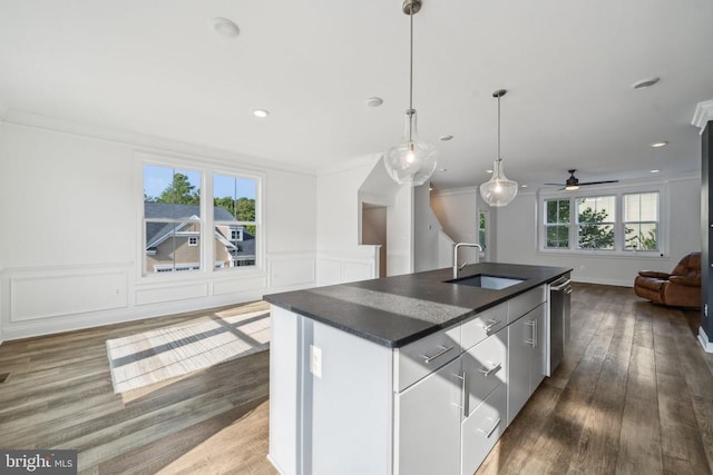 kitchen featuring open floor plan, a sink, dark countertops, stainless steel dishwasher, and a kitchen island with sink