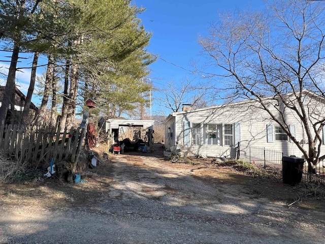 view of front of home with dirt driveway, fence, and a carport