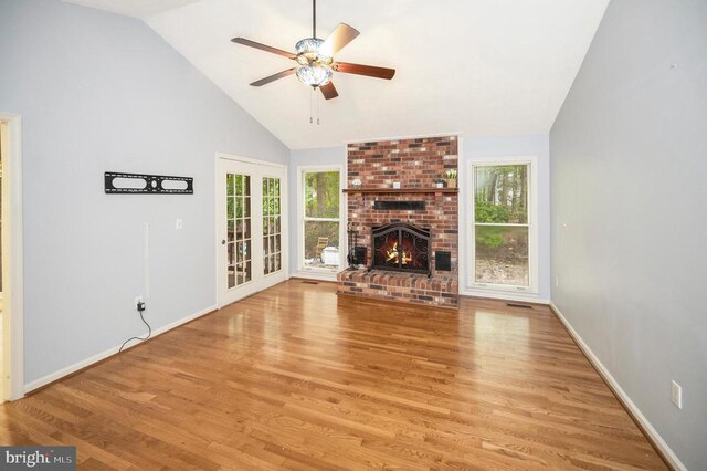 unfurnished living room featuring a ceiling fan, a brick fireplace, plenty of natural light, and wood finished floors