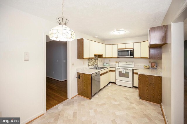 kitchen featuring a sink, light countertops, hanging light fixtures, baseboards, and appliances with stainless steel finishes