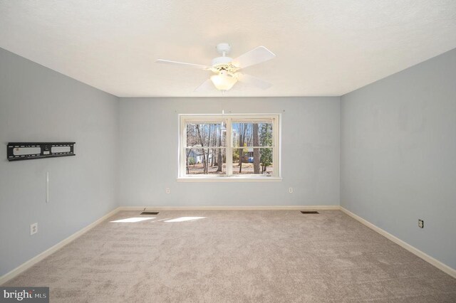 carpeted spare room with a ceiling fan and baseboards