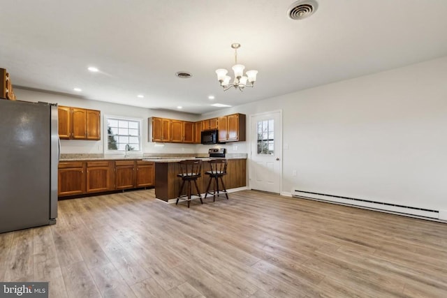 kitchen featuring stainless steel appliances, baseboard heating, light hardwood / wood-style floors, pendant lighting, and a kitchen bar