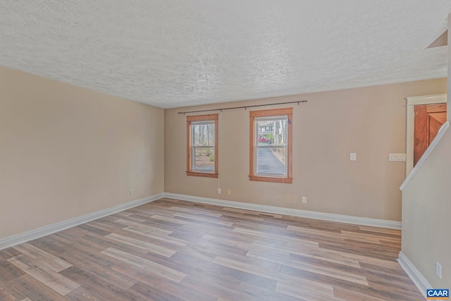 unfurnished room featuring a textured ceiling, light wood-style flooring, and baseboards