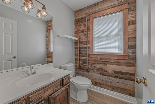 bathroom with wood walls, toilet, vanity, baseboards, and wood finished floors
