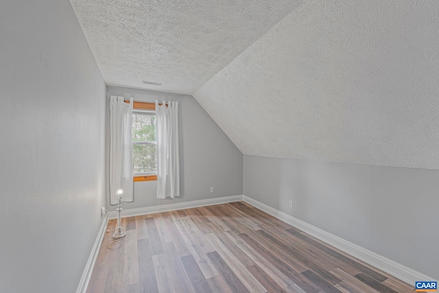 bonus room featuring a textured ceiling, wood finished floors, baseboards, and lofted ceiling