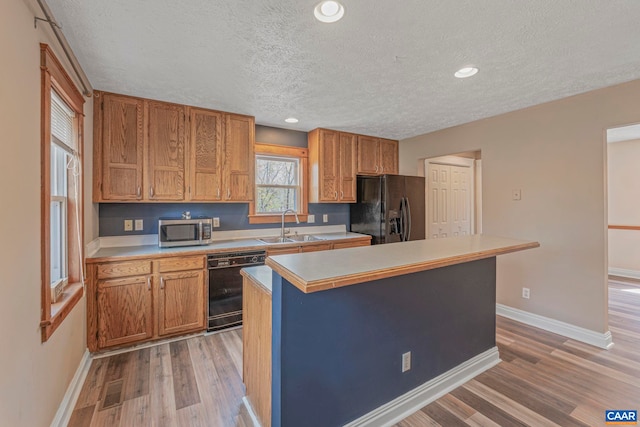 kitchen featuring black appliances, a sink, a textured ceiling, light countertops, and light wood finished floors