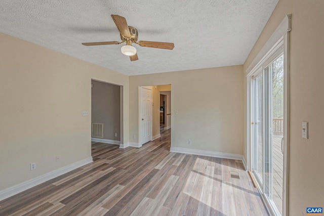 empty room with a textured ceiling, wood finished floors, baseboards, and ceiling fan