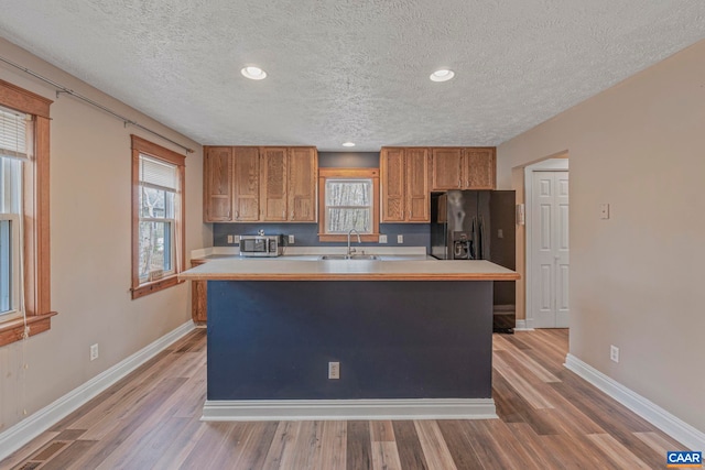 kitchen with brown cabinets, a textured ceiling, stainless steel microwave, baseboards, and black refrigerator with ice dispenser