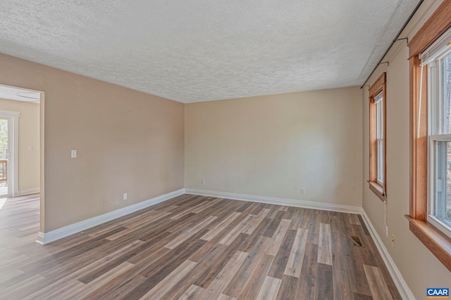 empty room featuring a textured ceiling, wood finished floors, and baseboards
