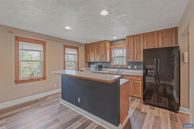kitchen with black refrigerator with ice dispenser, a sink, brown cabinets, light wood-type flooring, and a textured ceiling