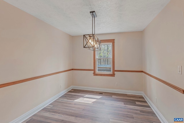empty room with wood finished floors, a chandelier, a textured ceiling, and baseboards